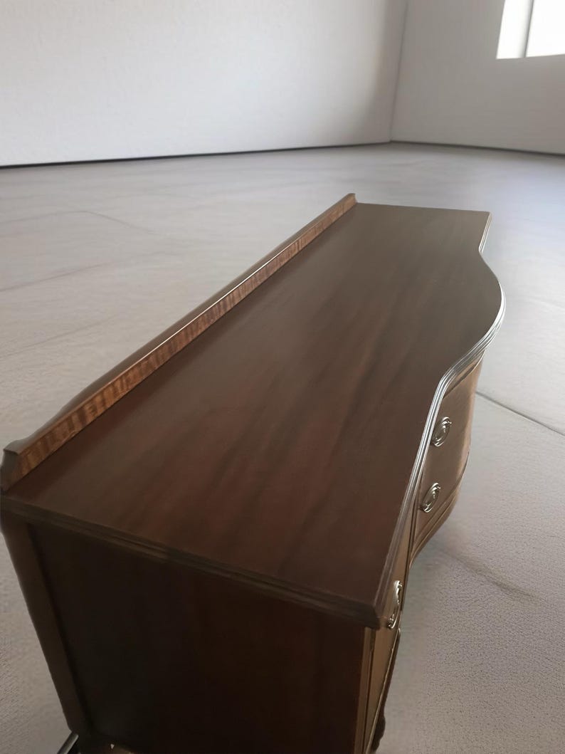May include: A dark brown wooden dresser with two drawers and a curved front. The dresser has brass hardware and a smooth, polished finish.