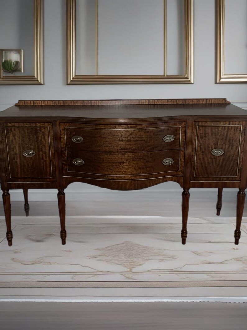 May include: A dark brown wooden buffet with a curved front and three drawers. The buffet has four legs and is sitting on a white rug.