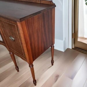 May include: A vintage wooden sideboard with a dark brown finish and turned legs. The sideboard has two doors and a drawer. The doors have a raised panel design and are accented with brass hardware.