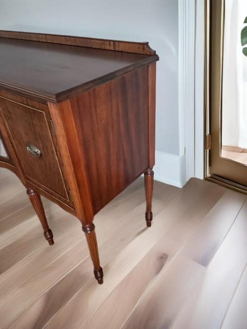 May include: A vintage wooden sideboard with a dark brown finish and turned legs. The sideboard has two doors and a drawer. The doors have a raised panel design and are accented with brass hardware.