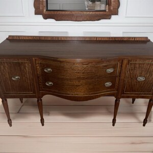 May include: A dark wood sideboard with two doors and two drawers. The sideboard has a curved front and sits on four legs.