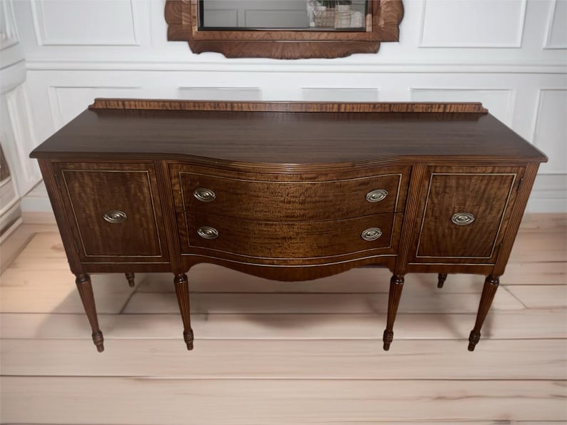 May include: A dark wood sideboard with two doors and two drawers. The sideboard has a curved front and sits on four legs.