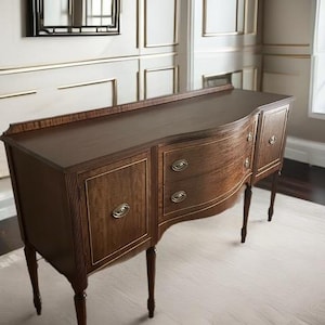 May include: A dark brown wooden sideboard with four doors and two drawers. The sideboard has a curved front and sits on four turned legs.