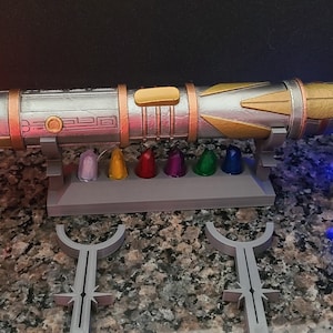 May include: A silver and gold lightsaber with a stand and seven colourful crystals. There is a red pyramid and a blue cube with geometric designs.