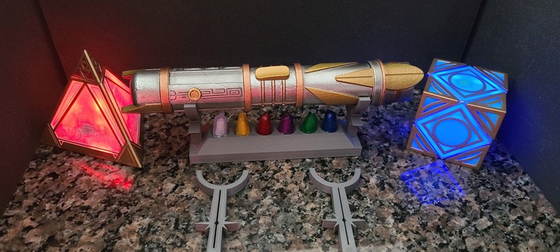 May include: A silver and gold lightsaber with a stand and seven colourful crystals. There is a red pyramid and a blue cube with geometric designs.
