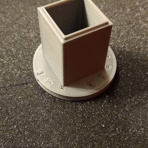 Pu&ograve; includere: Un cubo bianco stampato in 3D con una base circolare. La base ha i numeri da 1 a 10 stampati attorno al bordo.