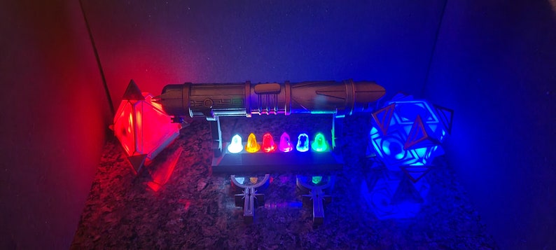 May include: A collection of colourful light-up toys, including a lightsaber, a crystal, and a cube. The lightsaber is black and silver, the crystal is red, and the cube is blue.