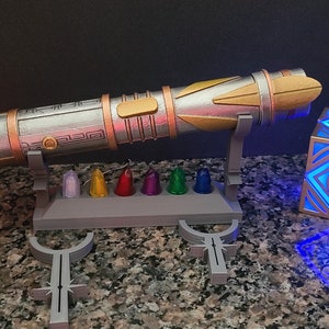 May include: A silver and gold lightsaber with a stand and a set of colourful crystals. There is a red pyramid-shaped light and a blue cube-shaped light.