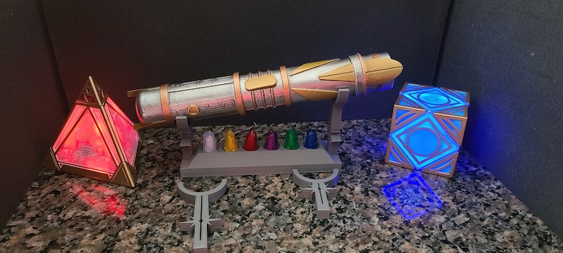 May include: A silver and gold lightsaber with a stand and a set of colourful crystals. There is a red pyramid-shaped light and a blue cube-shaped light.