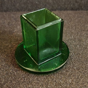 Pu&ograve; includere: Un contenitore quadrato in vetro verde con una base rotonda. Il contenitore &egrave; in vetro trasparente con una tinta verde.