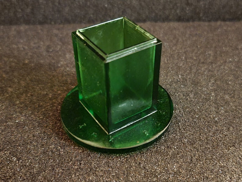 Pu&ograve; includere: Un contenitore quadrato in vetro verde con una base rotonda. Il contenitore &egrave; in vetro trasparente con una tinta verde.