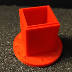 Pu&ograve; includere: Un calamaio di plastica arancione brillante con un'apertura quadrata e una base rotonda. La base ha le parole "INK" e "RULER" stampate su di essa.