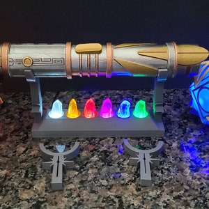 May include: A silver and gold lightsaber with a decorative stand, a red crystal, and a blue crystal. The stand has seven small crystals in various colours.