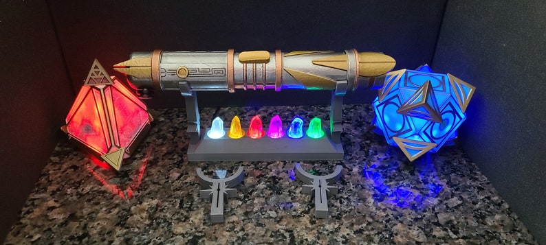 May include: A silver and gold lightsaber with a decorative stand, a red crystal, and a blue crystal. The stand has seven small crystals in various colours.
