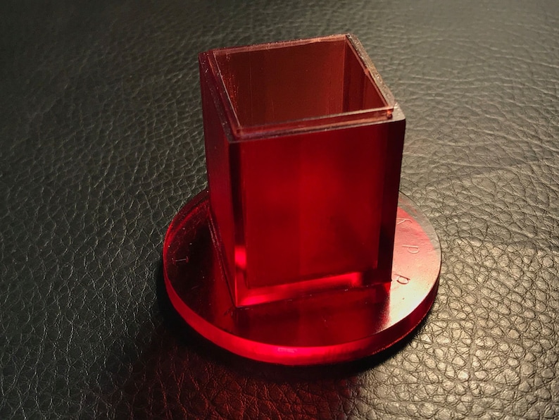 Pu&ograve; includere: Un cubo di acrilico rosso con una base quadrata si trova su una base circolare in acrilico rosso.