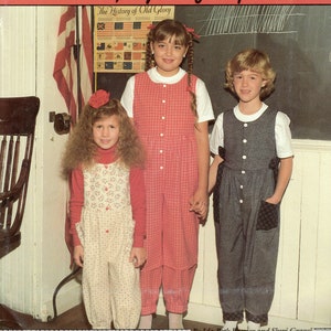 May include: A sewing pattern for a child's jumpsuit, called "Little Ginger's Jumpsuit." The pattern is for sizes 4-12 and is sewn entirely on the sewing machine. The pattern is illustrated with two children wearing the jumpsuit, one in red and white plaid and the other in gray and white.