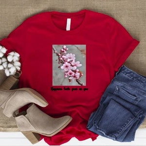 May include: A red t-shirt with a floral graphic and the text "Happiness looks great on you." The shirt is paired with blue jeans and beige ankle boots. Cotton flowers are also in the image.