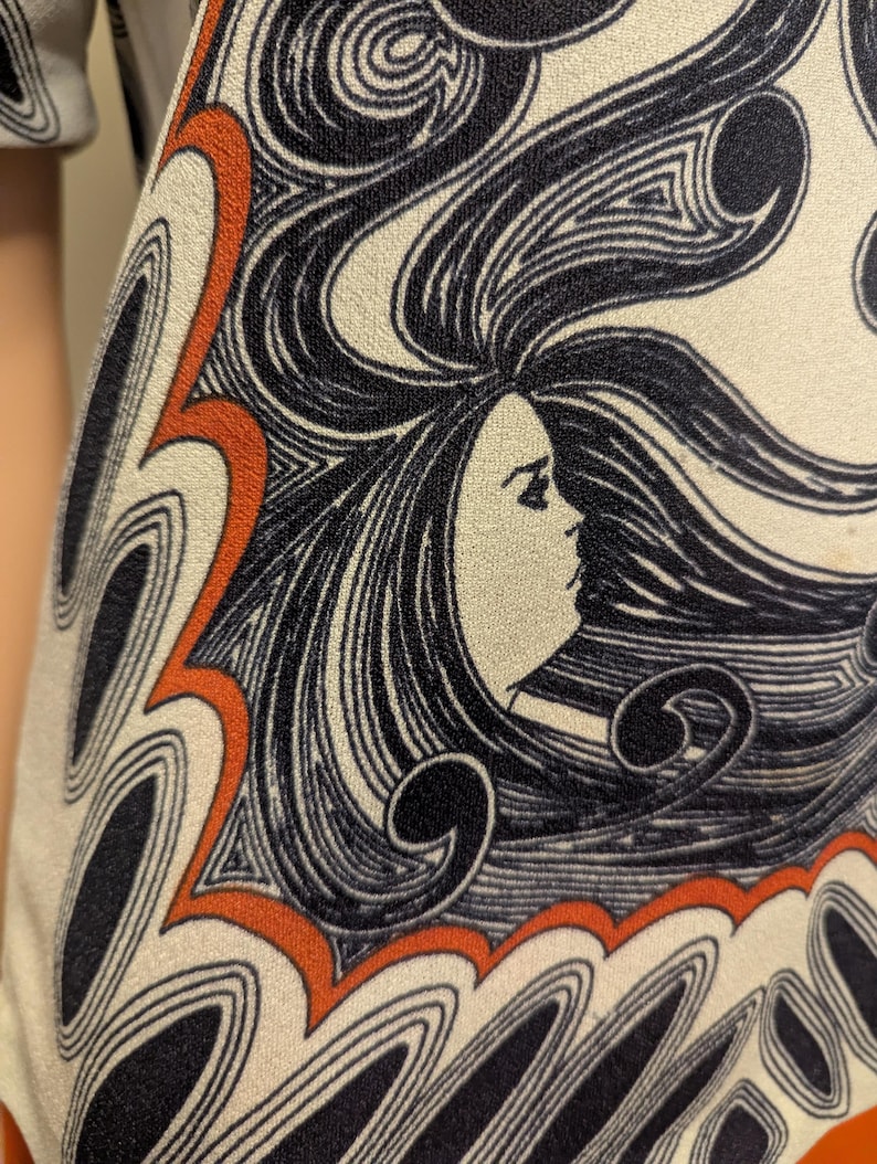 Pu&ograve; includere: Primo piano di un tessuto color crema con un motivo ripetuto. Il design presenta il profilo di una donna con capelli neri fluenti ed elementi decorativi arancioni e neri. Il tessuto sembra far parte di un capo d'abbigliamento, con un'estetica vintage.