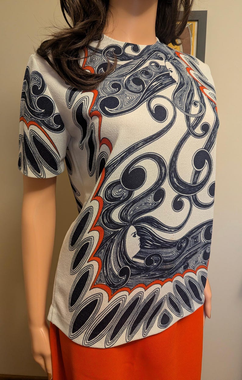 Pu&ograve; includere: Top bianco a maniche corte con un motivo ripetuto di volti femminili stilizzati e capelli fluenti in blu navy e rosso. Il top &egrave; abbinato a una gonna arancione, creando un contrasto sorprendente.