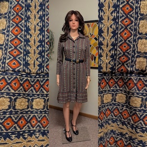 May include: A vintage button-down dress with a geometric pattern in brown, red, and beige. The dress has long sleeves, a collar, and a black belt. The dress is knee-length and is displayed on a mannequin.
