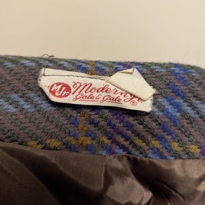 Pu&ograve; includere: Primo piano di un tessuto vintage con etichetta Modern Gale & Gale. Il tessuto presenta un motivo intrecciato nelle tonalit&agrave; del blu, viola e giallo. L'etichetta &egrave; bianca con testo rosso.
