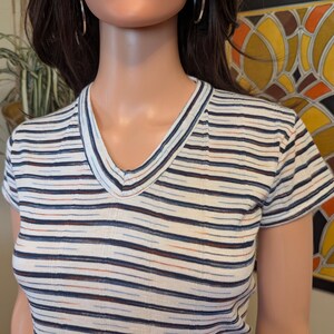 May include: A white striped short-sleeved shirt with a v-neck. The stripes are blue, orange, and brown.