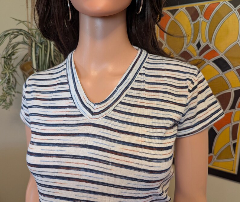 May include: A white striped short-sleeved shirt with a v-neck. The stripes are blue, orange, and brown.