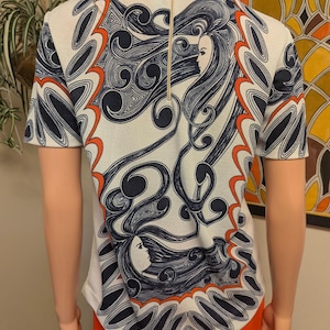 Pu&ograve; includere: Top color crema a maniche corte con un design sorprendente con motivi a spirale blu navy e arancioni e il profilo di un volto femminile. Il top ha una cerniera dorata sul retro.