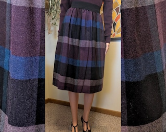 May include: A vintage plaid skirt in shades of purple, blue, and black. The skirt has a high waist with a black elastic band and a pleated design. The model is wearing a matching purple sweater and black heels.