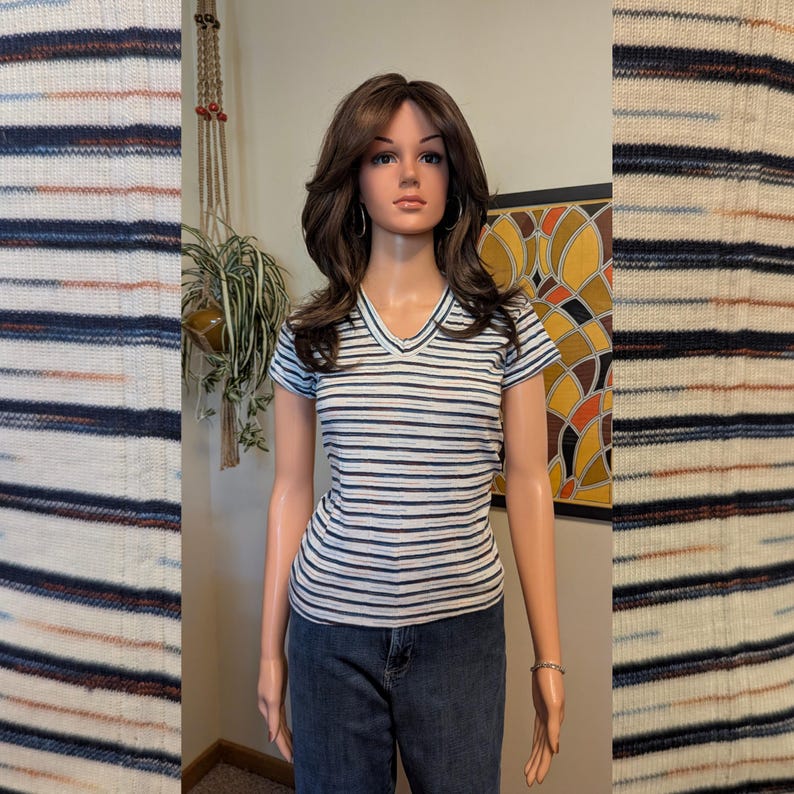 May include: A white striped short-sleeved shirt with a v-neck. The shirt has thin blue, orange, and black stripes. The shirt is being modeled by a mannequin.