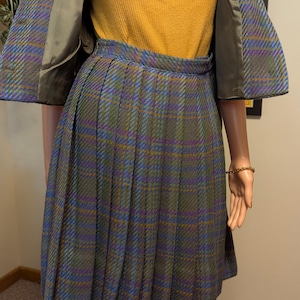 Pu&ograve; includere: Un completo gonna vintage a quadri, con gonna plissettata e giacca abbinata. La combinazione di colori comprende verde, blu, viola e giallo. L'outfit &egrave; abbinato a un top a coste giallo senape.