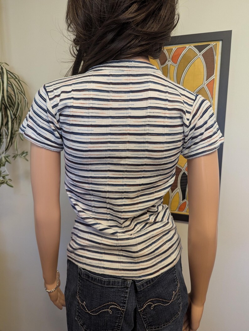 May include: A white striped short-sleeved shirt with blue, brown, and red stripes. The shirt is fitted and has a round neckline.