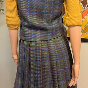 Pu&ograve; includere: Completo gonna vintage a quadri con gonna a pieghe e gilet abbinato. Il gilet e la gonna sono un mix di blu, verde e viola. Sotto &egrave; indossato un maglione giallo senape.