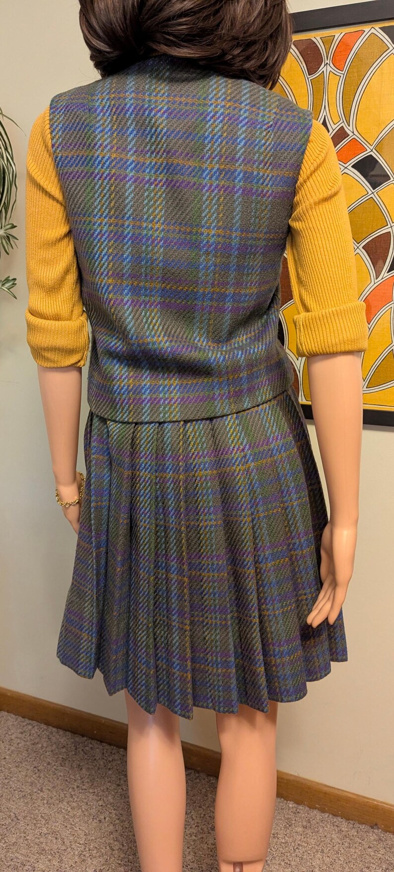 Pu&ograve; includere: Completo gonna vintage a quadri con gonna a pieghe e gilet abbinato. Il gilet e la gonna sono un mix di blu, verde e viola. Sotto &egrave; indossato un maglione giallo senape.