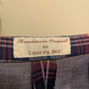 Op de afbeelding: Een close-up van een geruite stof met een wit label waarop "Handmade Original by Lauryn Bell" staat.