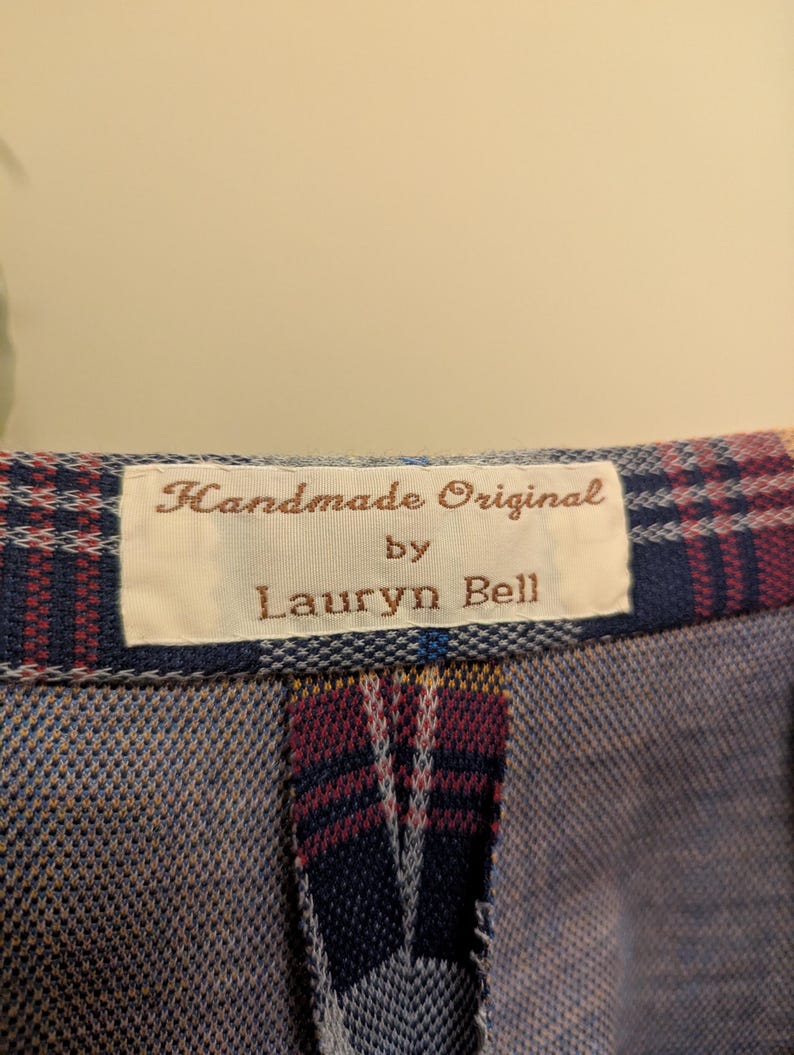 Op de afbeelding: Een close-up van een geruite stof met een wit label waarop "Handmade Original by Lauryn Bell" staat.