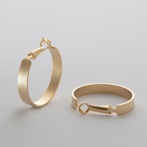 May include: A pair of gold hoop earrings with a brushed finish. The earrings have a hinged closure.