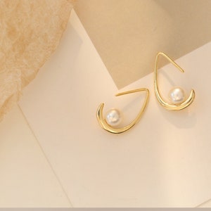 May include: A pair of gold hoop earrings with a single pearl accent on each hoop.