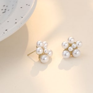 Puede incluir: Un par de pendientes de botón de tono dorado con un racimo de perlas blancas en forma de flor.