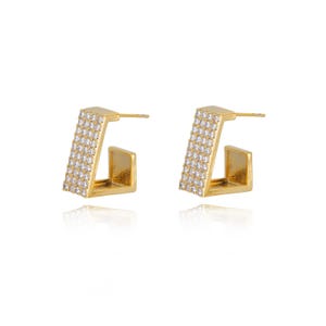 May include: A pair of gold-colored, geometric hoop earrings. The earrings have a rectangular shape with a section of small, clear stones. The earrings are displayed on a white background.