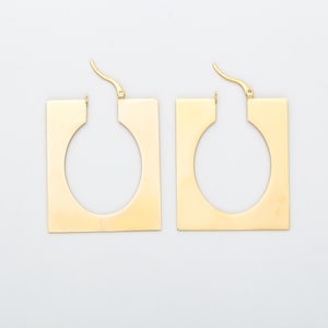 May include: A pair of gold square hoop earrings with a circular cutout in the center.