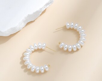 May include: A pair of gold hoop earrings with white pearl beads. The earrings are simple and elegant.