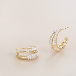 May include: A pair of gold hoop earrings with a triple row of white pearls.