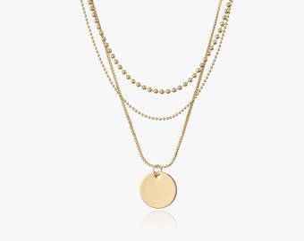May include: Gold layered necklace with a round pendant. The necklace has three chains of different sizes and styles.
