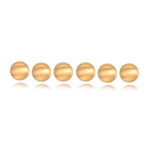 May include: Six gold-colored, round stud earrings are arranged in a horizontal line against a white background. The earrings have a brushed metal finish, reflecting light. The jewelry is simple and elegant.