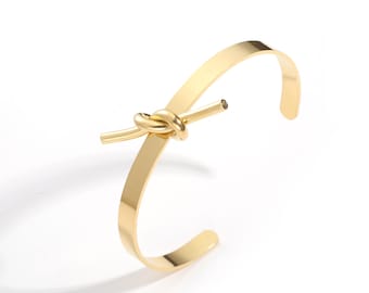 Peut inclure: Un bracelet en métal doré avec un motif de nœud. Le bracelet est ouvert et réglable.