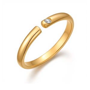 May include: A gold-colored ring with a small, clear gemstone set into one end. The ring has an open design, with a gap between the two ends. The ring is set against a white background.
