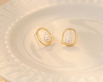 Könnte beinhalten: Ein Paar goldfarbene Ohrringe mit einem einfachen ovalen Design und einer einzelnen Perle in jedem Ohrring.