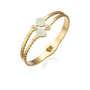 May include: Gold-toned bracelet featuring a twisted rope design. The bracelet has two parallel bands with a clasp closure. It is adorned with two seashell-shaped charms in white and light green, each accented with a small pearl.