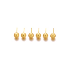 May include: Six gold-toned stud earrings, each featuring a spherical ball with a textured, glittery finish. Each earring has a thin, straight post extending from the back of the round, metallic bead, designed for secure placement in an earlobe.